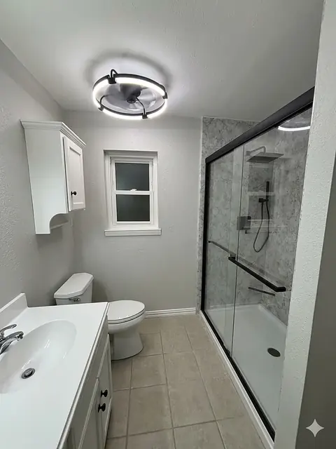 Tub-to-Shower Conversion — tub-to-shower conversion with soft grey stone panels, a black-framed sliding glass door, low-threshold base and matching grab bar, installed by Revive Bath Solutions in Longview, TX